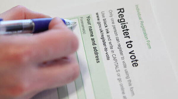 Person using a blue pen to fill-in a voter registration form